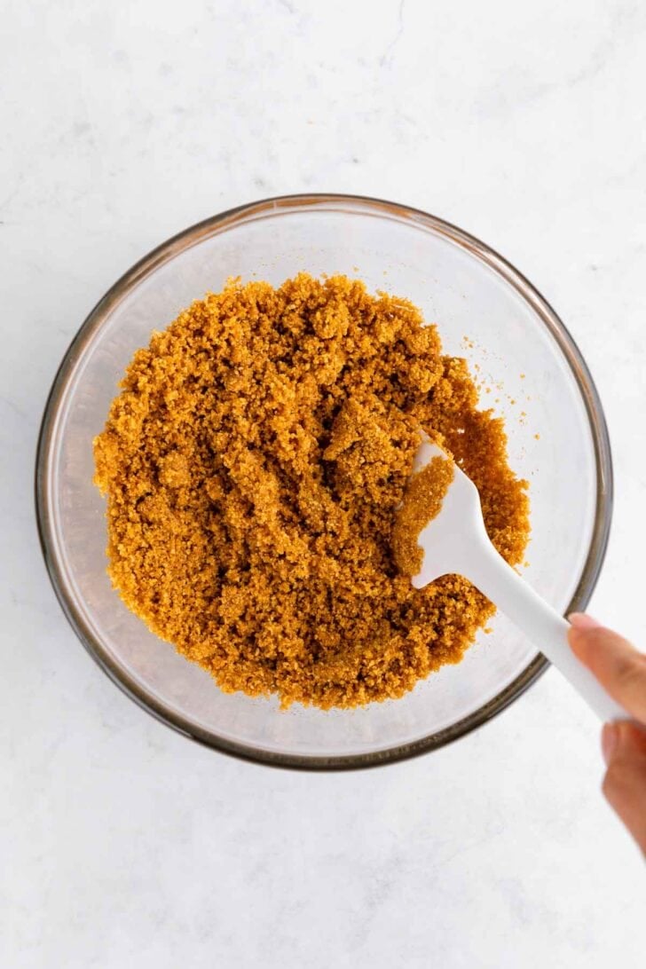 mixing graham cracker crumbs and melted butter in a glass bowl with a rubber spatula