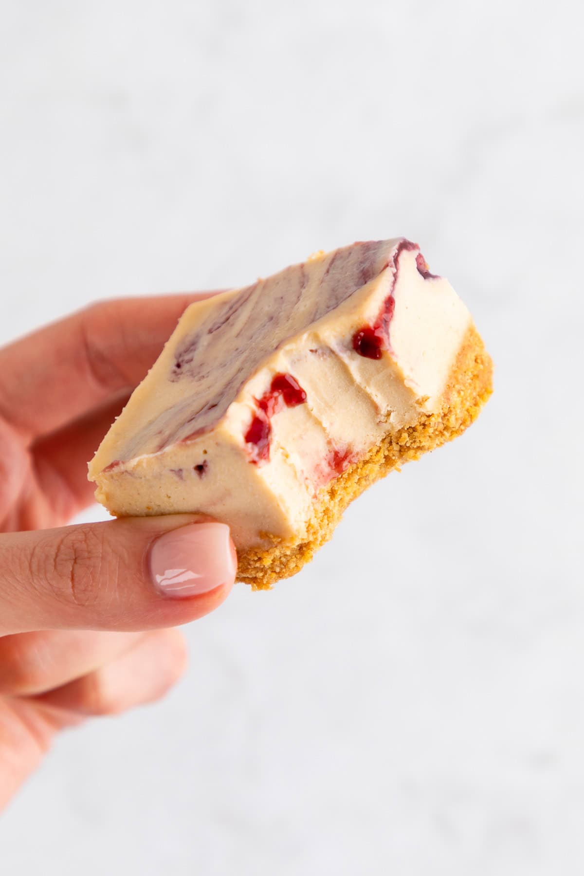 a hand holding a no-bake peanut butter and jelly cheesecake bar with a bite taken out of it