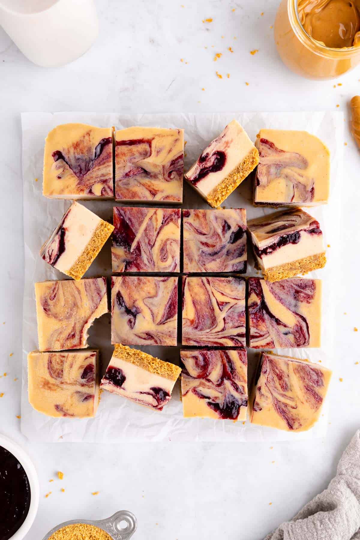 a pile of no-bake peanut butter and jelly cheesecake bars with a berry swirl